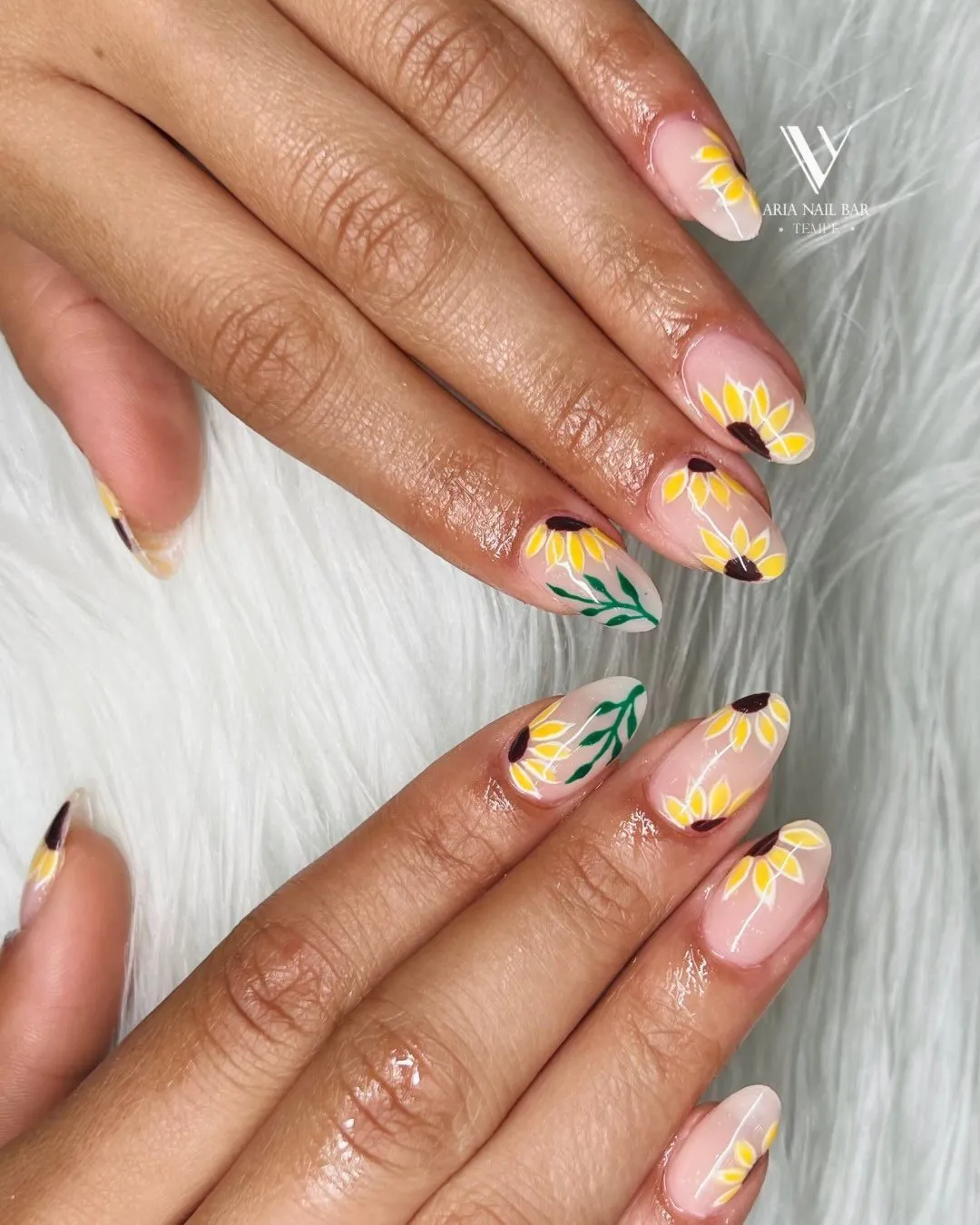 Nude nails with hand-painted sunflowers and green leaves on the accent fingers.