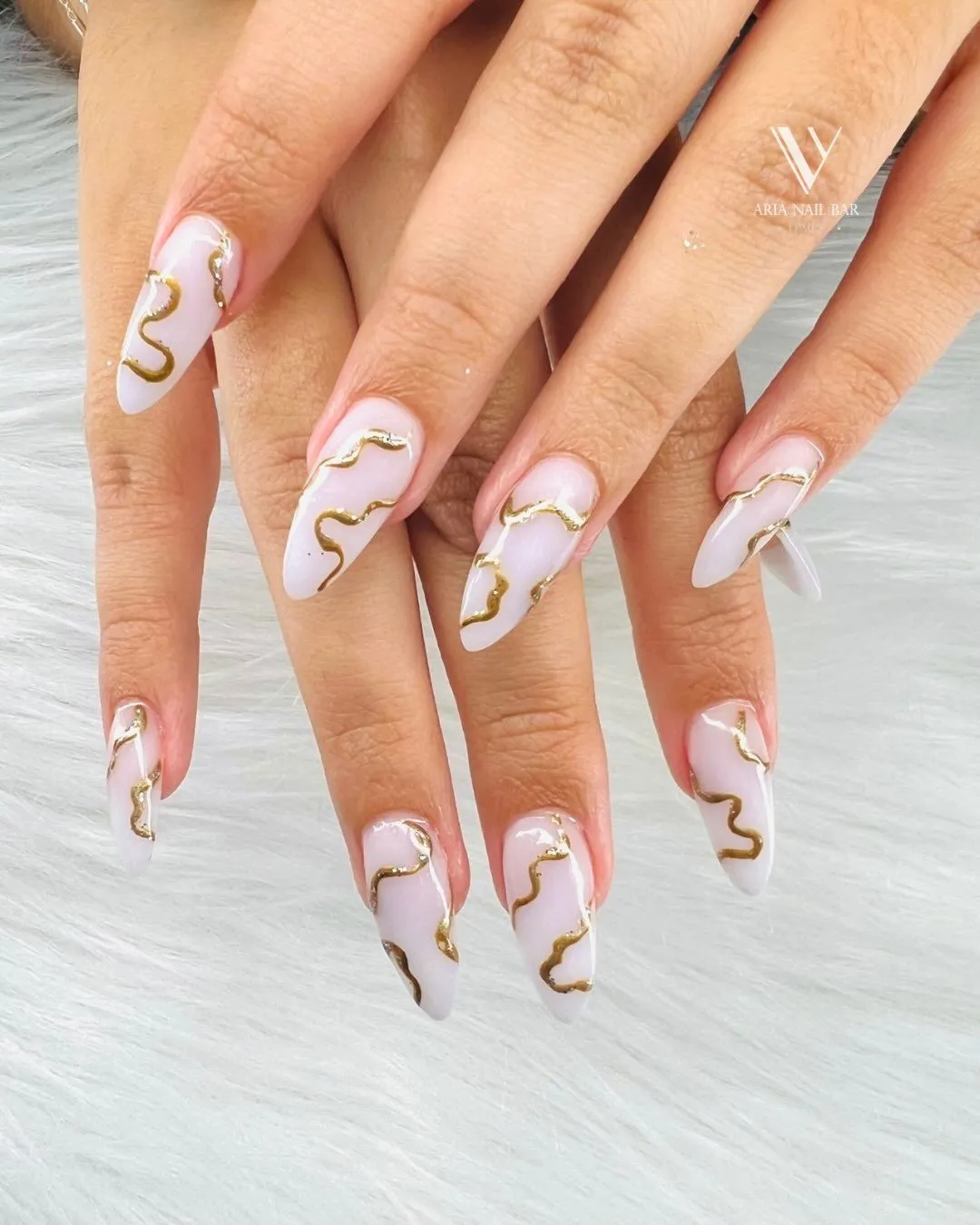 Milky white almond nails with hand-painted gold swirl accents.